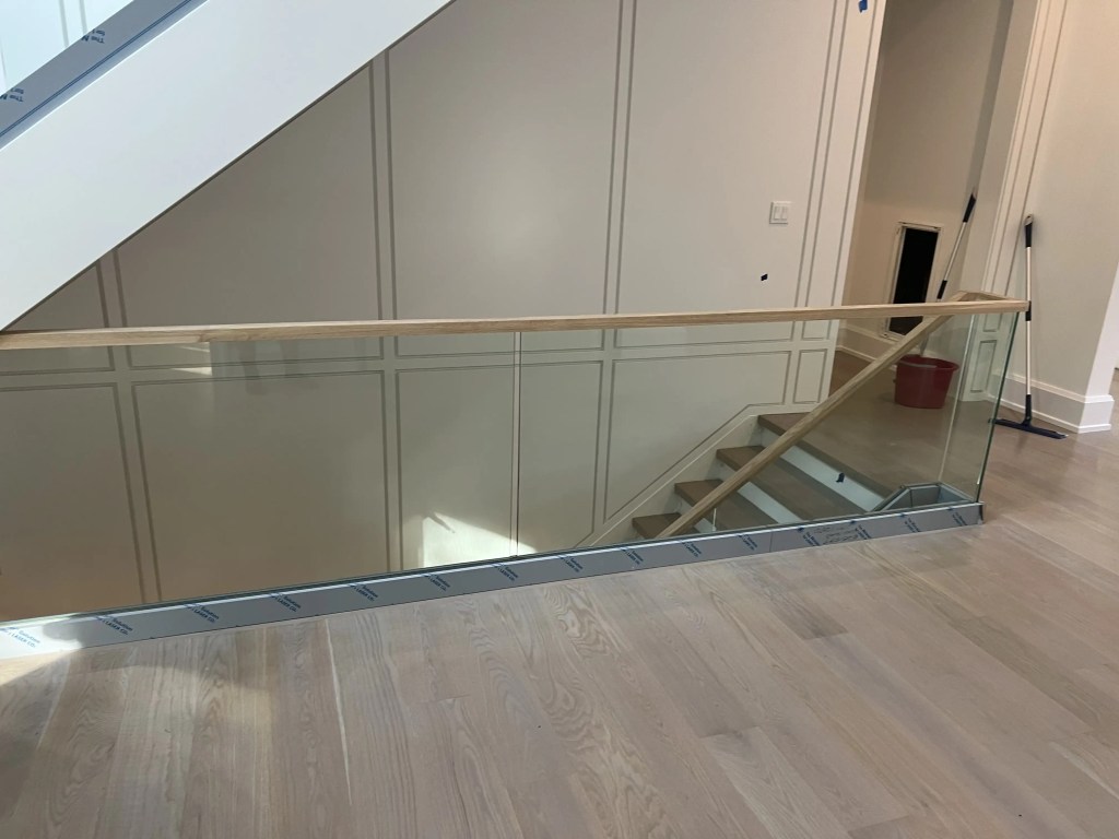 Elegant glass and wood staircase railing with handrail for modern interiors.