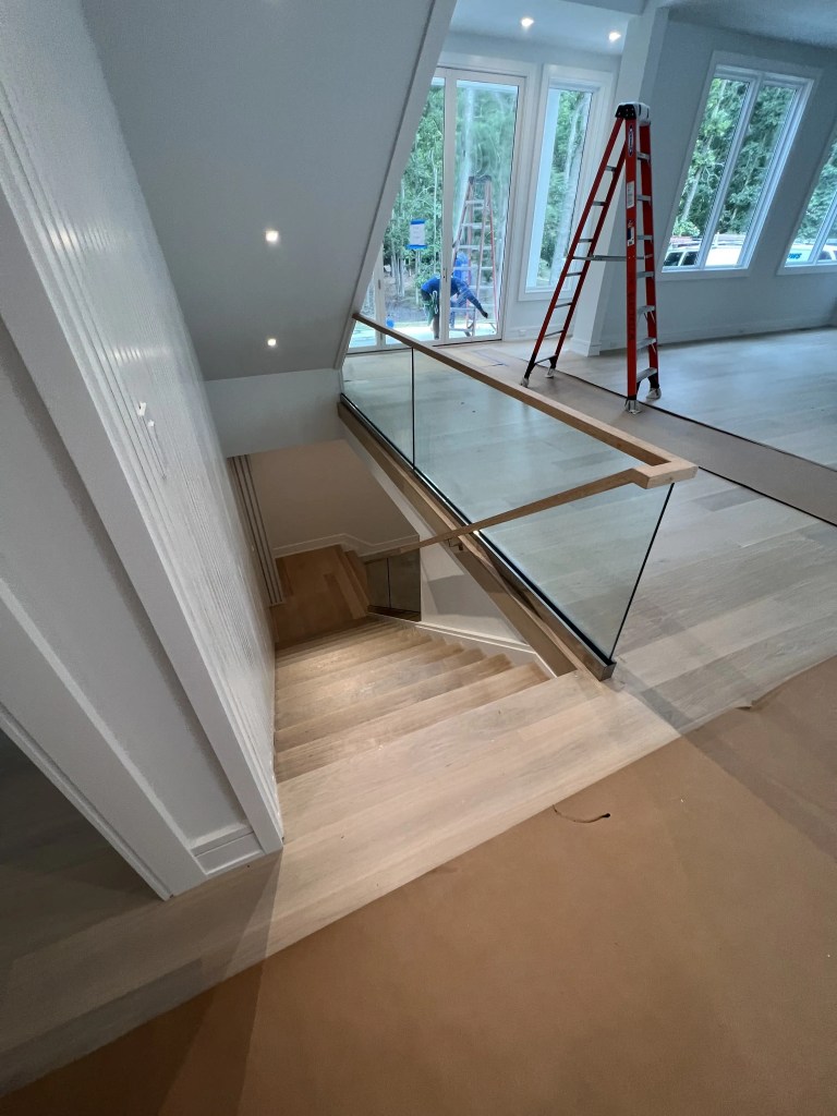 Elegant glass railing with wood finish for staircase and balcony in a contemporary home.
