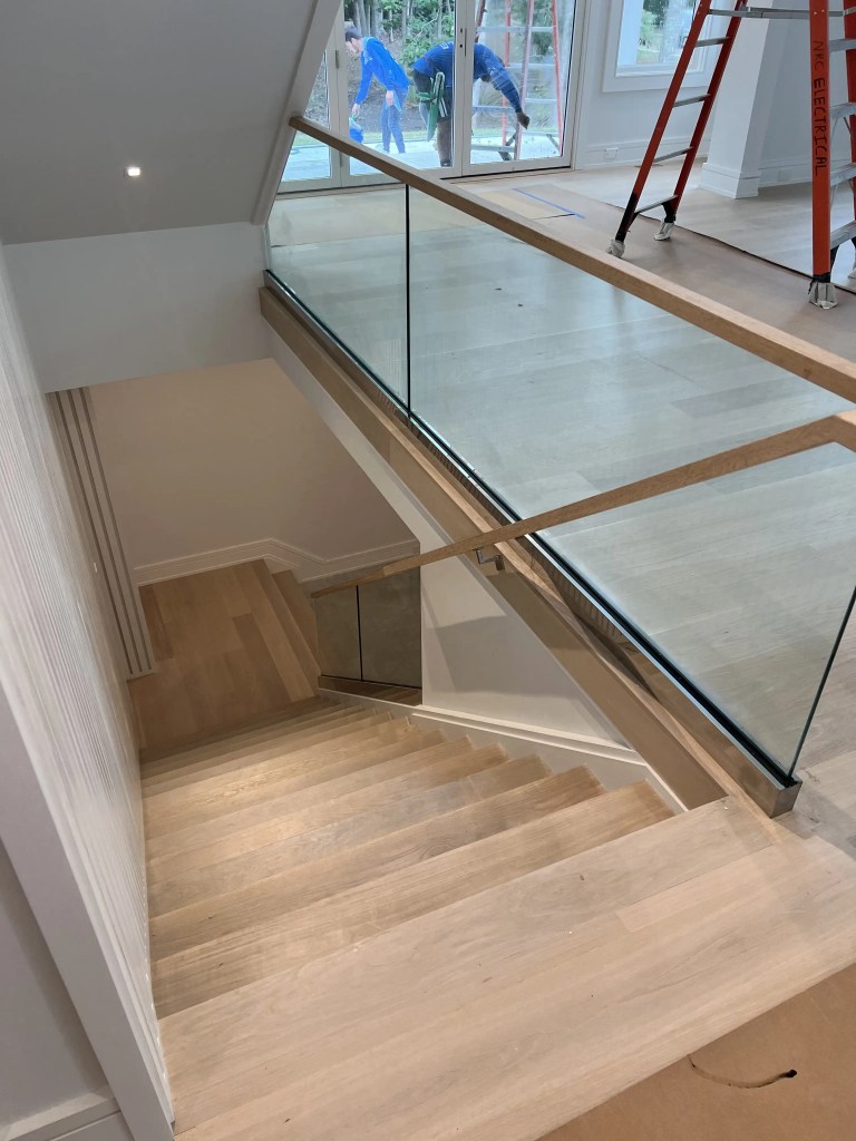 Wood staircase with glass railing and wood finish, showcasing elegant home interior design.